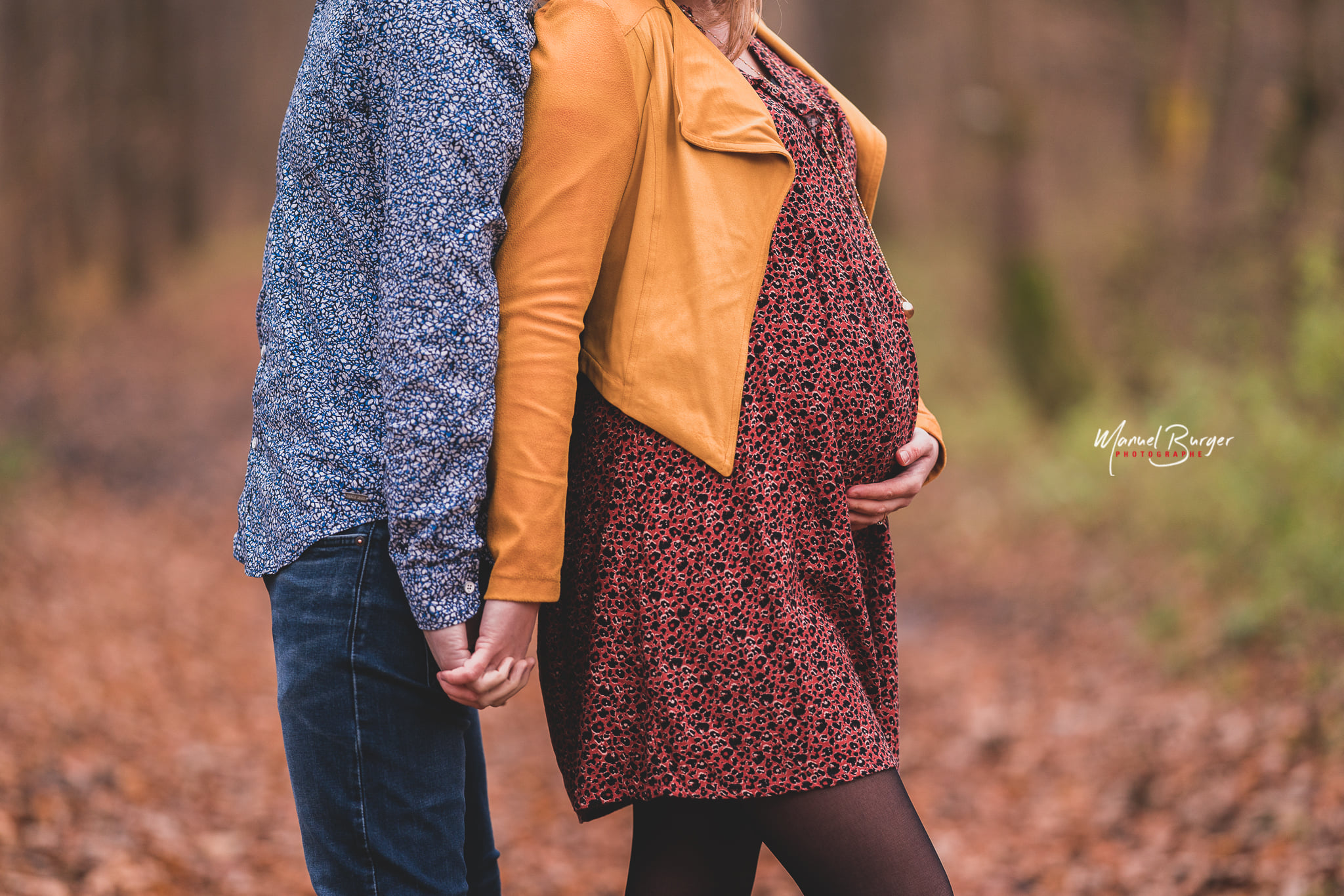 Gros plan sur le ventre arrondi d'une future maman posant dos à dos avec le futur papa lors d'une séance photo de grossesse dans la forêt de l'Illwald près de Sélestat.