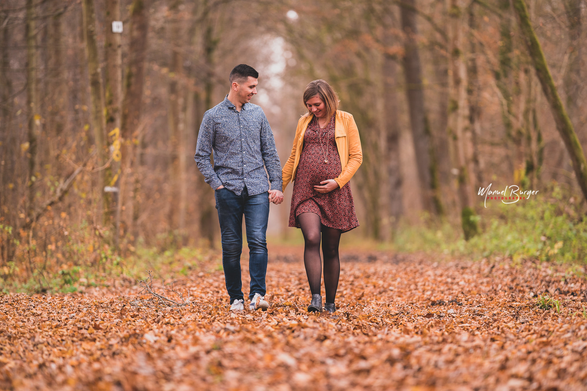 Couple complice marchant main dans la main sur un sentier forestier en automne pour leur reportage photo de grossesse dans la nature sélestadienne.