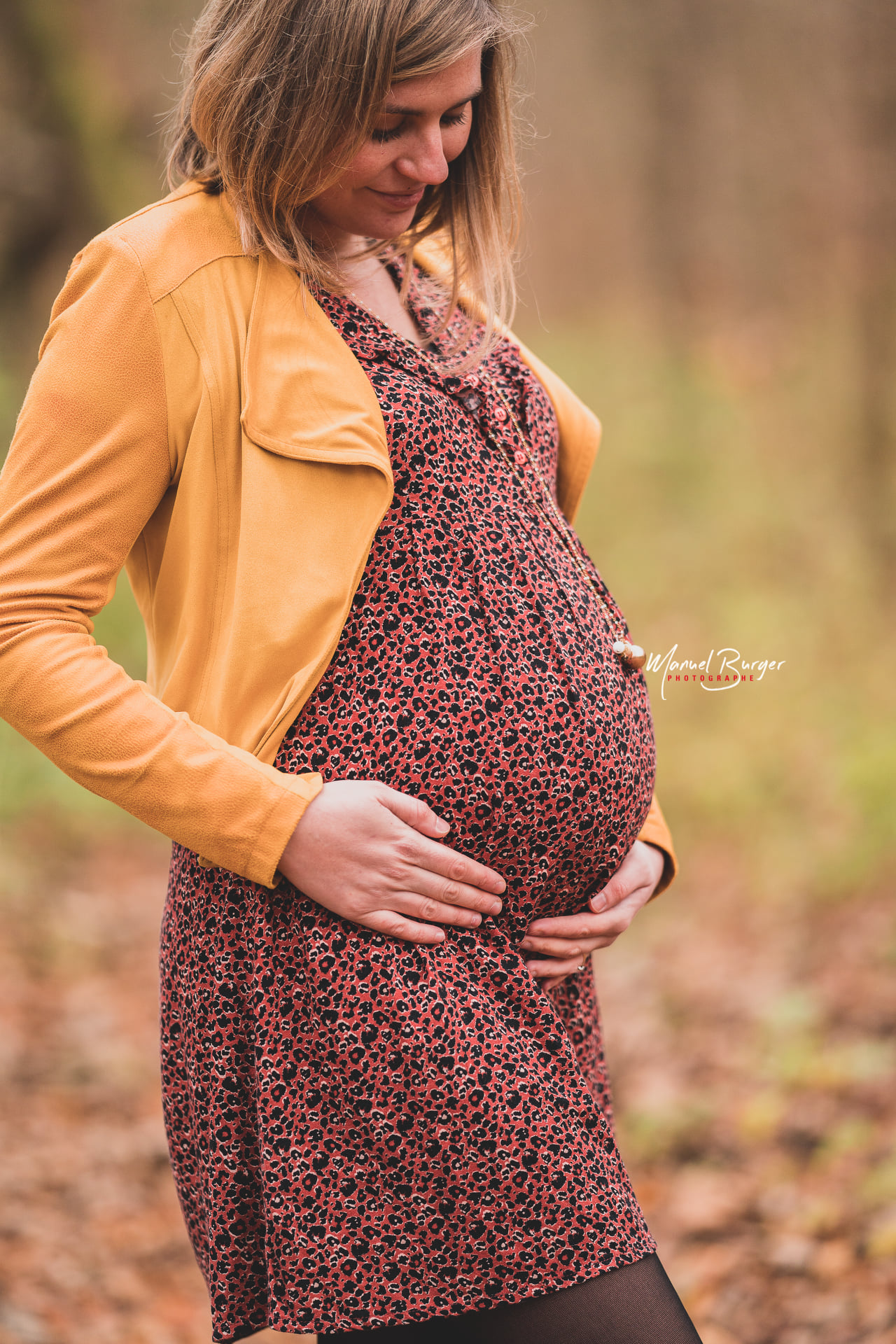 Doux portrait d'une future maman regardant tendrement son ventre pendant une séance photo de maternité en extérieur dans les forêts d'Alsace.