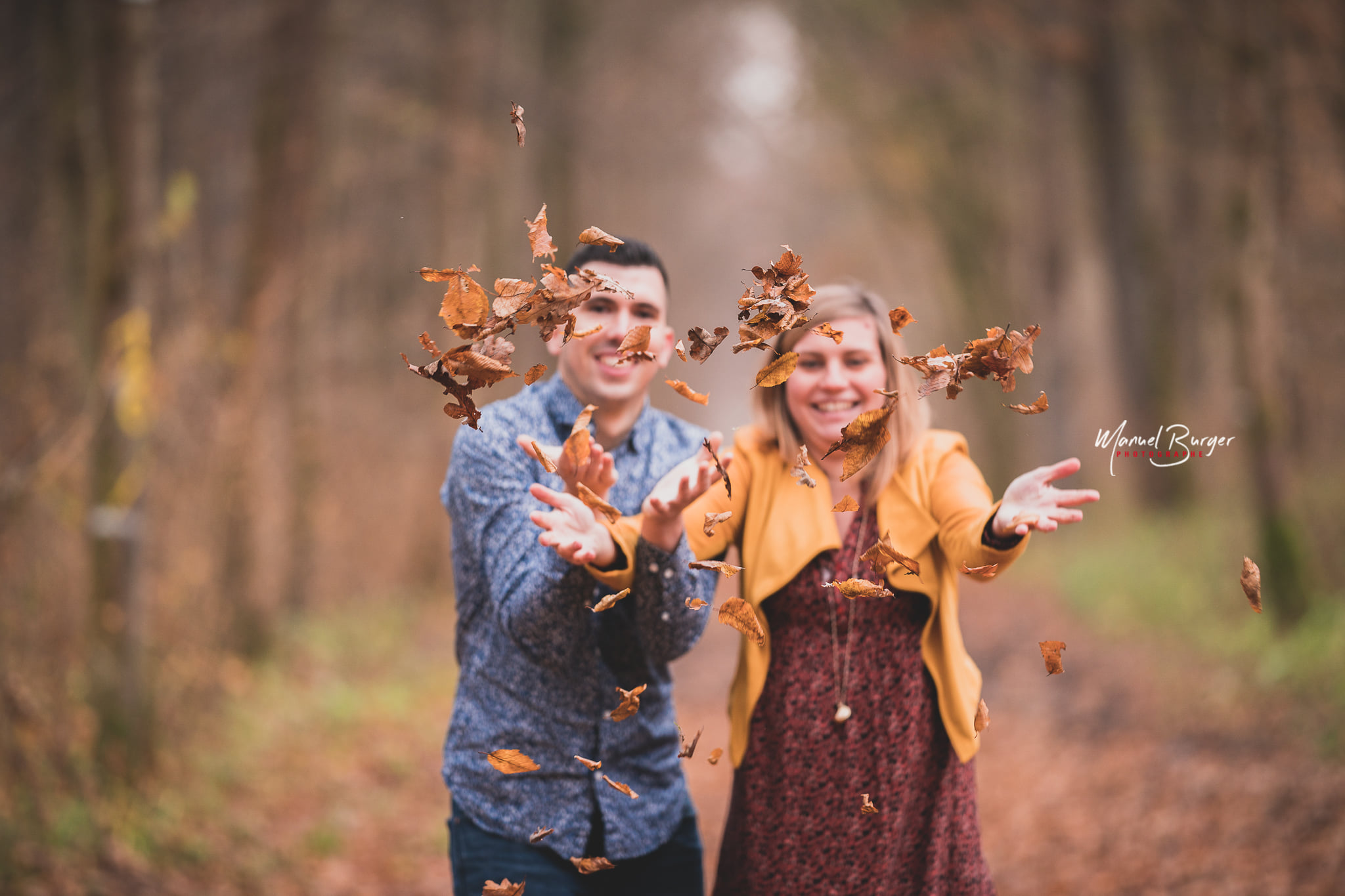 Les futurs parents s'amusent et lancent des feuilles d'automne vers l'objectif du photographe de maternité lors d'une balade dans le Ried.